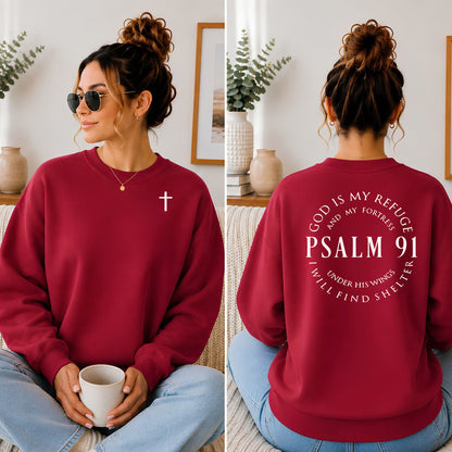 A woman shown in a split front-and-back view wearing a burgundy crewneck sweatshirt. The front view shows a small white cross on the left chest, and the back view shows a large white circular Bible verse print reading 'PSALM 91'.
