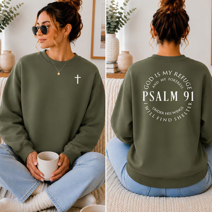 An olive green crewneck sweatshirt shown on a model in a split front and back view. The front features a small white cross on the left chest, and the back features a large white circular graphic reading 'GOD IS MY REFUGE AND MY FORTHNESS PSALM 91 I WILL FIND SHELTER'.